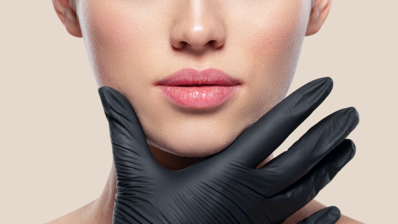 Kobieca broda podtrzymywana dłonią w czarnej rękawiczce